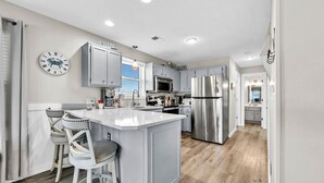 Een moderne keuken met een centraal eiland, roestvrijstalen apparatuur en een klok aan de muur.