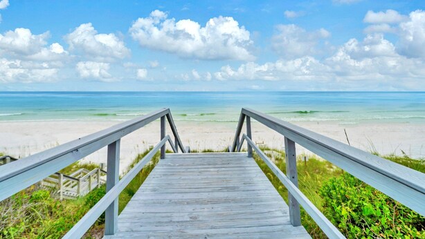 Une promenade en bois qui mène à une plage, avec un ciel dégagé et une mer calme.