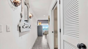 Un pasillo con diseño moderno, que presenta un suelo de tonos claros, paredes blancas y una puerta con persianas horizontales.