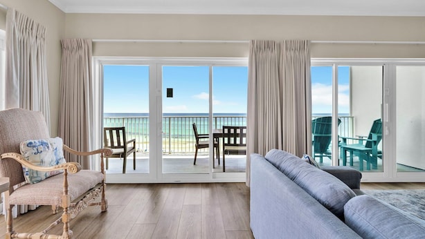 Une pièce avec un plancher en bois, un canapé gris, une chaise en bois et un balcon donnant sur la plage.