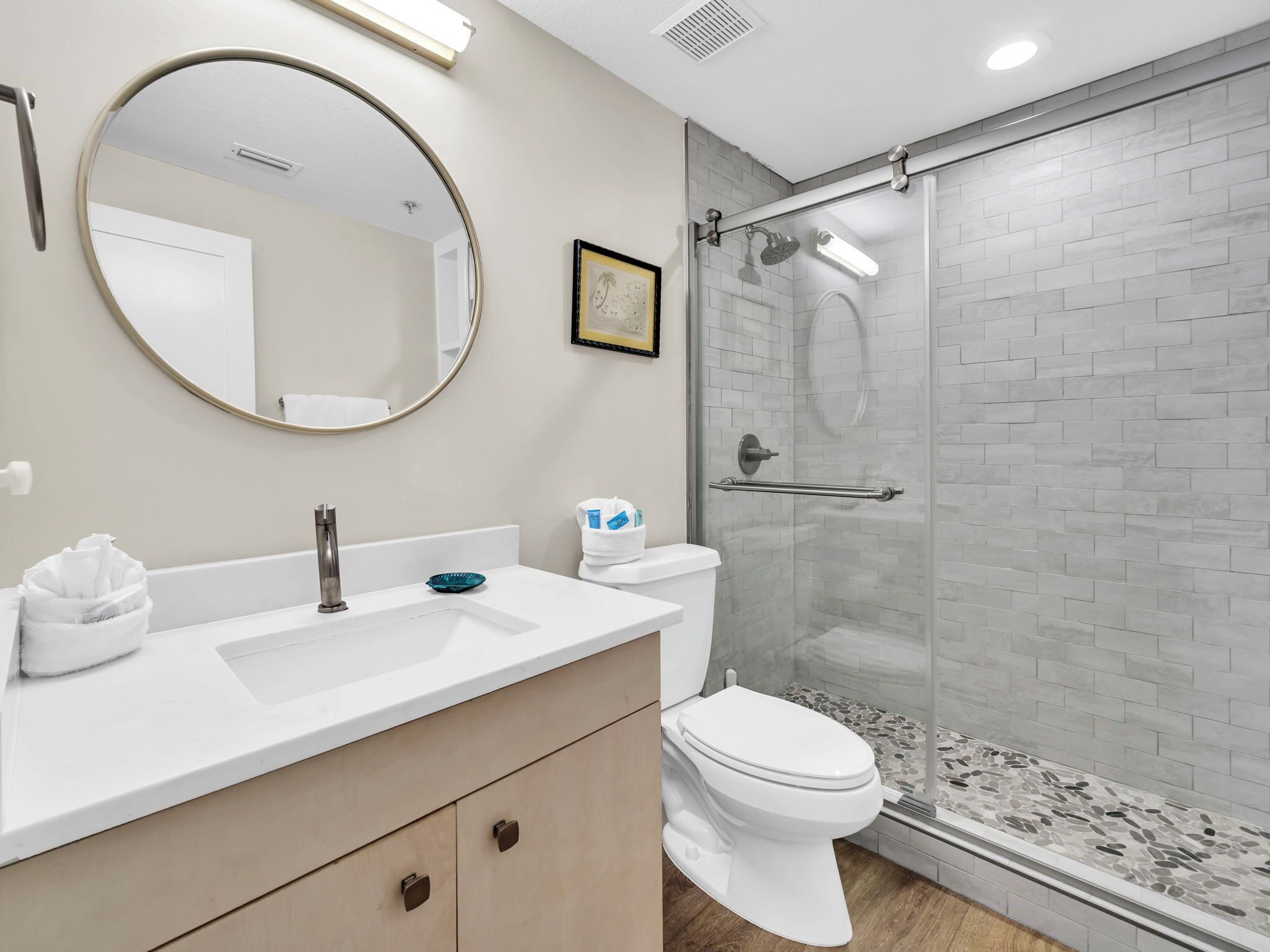 A modern bathroom with a round mirror, a sink, a toilet, and a glass-enclosed shower.
