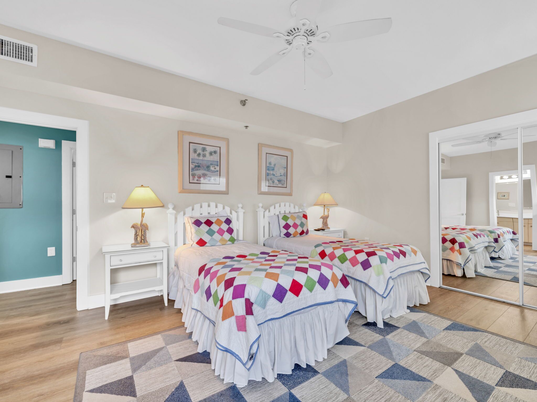 A bedroom with two beds, a ceiling fan, a large mirror, and a patterned rug.