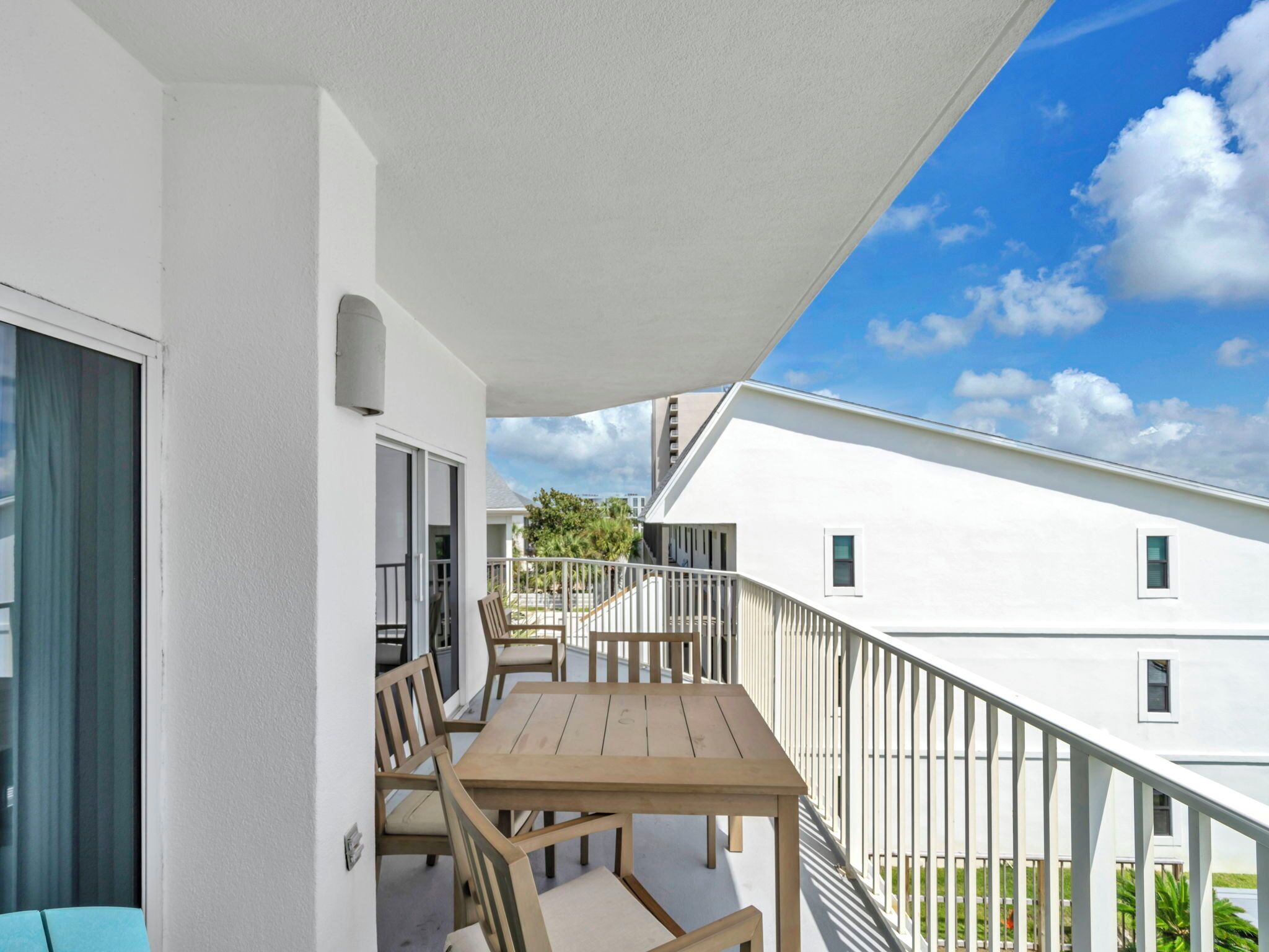 Ein Balkon mit Holztisch und -stühlen, weißen Wänden und blauem Himmel mit Wolken.