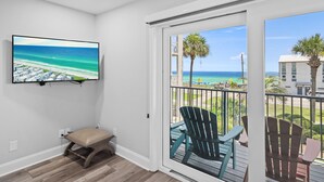 Un balcon avec vue sur l’océan et la plage, un téléviseur fixé au mur et un banc.