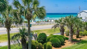 Une vue sur la côte, avec des palmiers, une route et une plage parsemée de parasols.