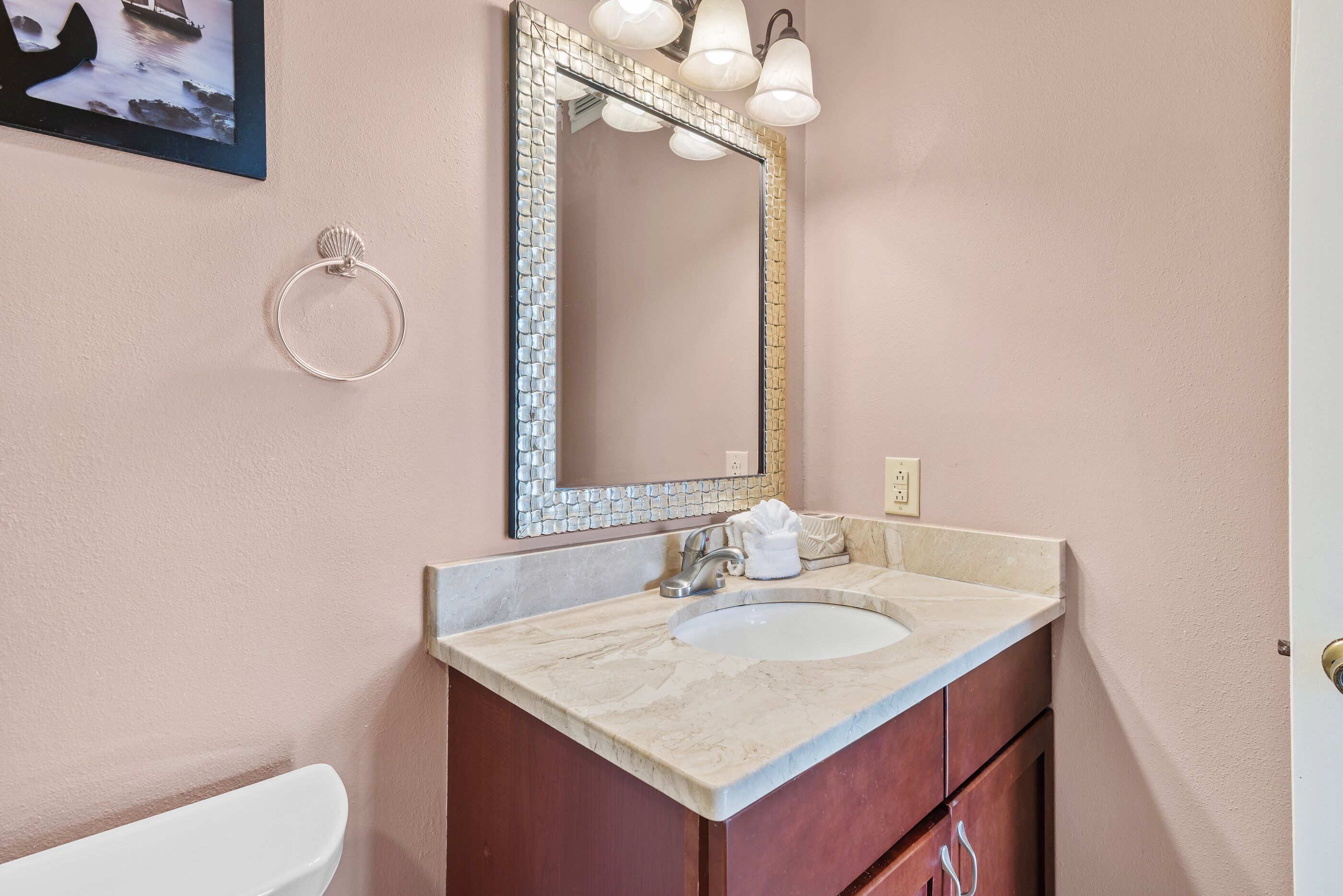 A bathroom with a marble sink, a mirror with mosaic trim, and a ring-shaped towel holder on the wall.