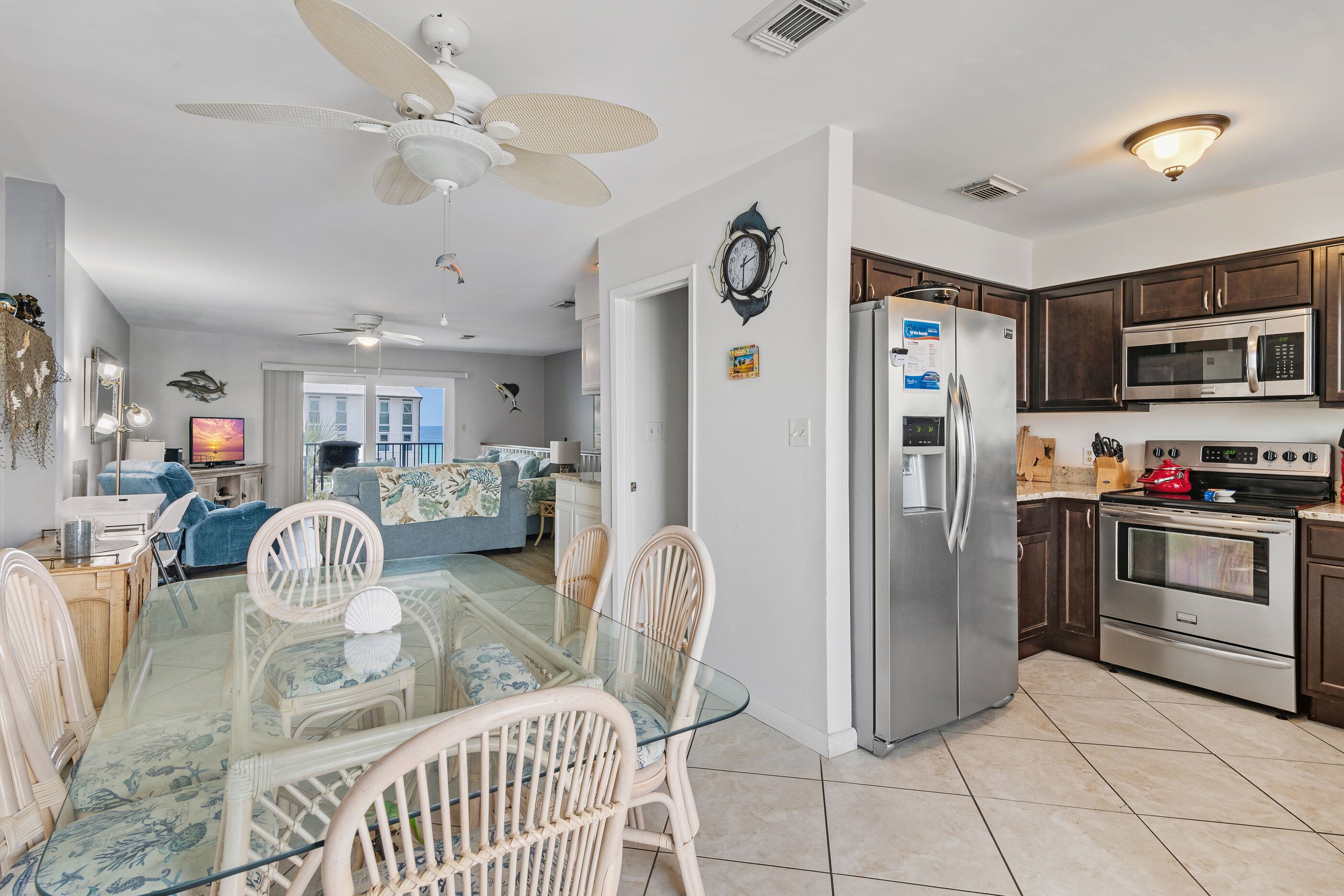 A spacious kitchen with modern appliances, a dining area with glass-top table and wicker chairs, and a ceiling fan.