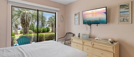 A bedroom with a bed, a dresser, a TV, and a view of the outdoors.
