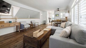 Un salón amplio con un sofá gris, una mesa de centro de madera y un televisor montado en la pared.