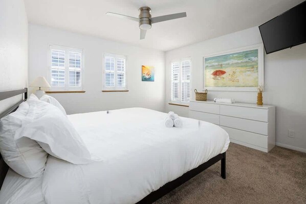 A bedroom with a bed, a ceiling fan, a dresser, and a painting on the wall.