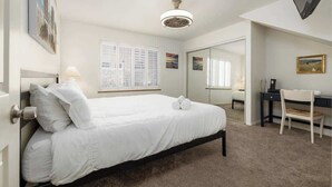 Un dormitorio con cama, escritorio, silla, espejo y ventilador de techo.