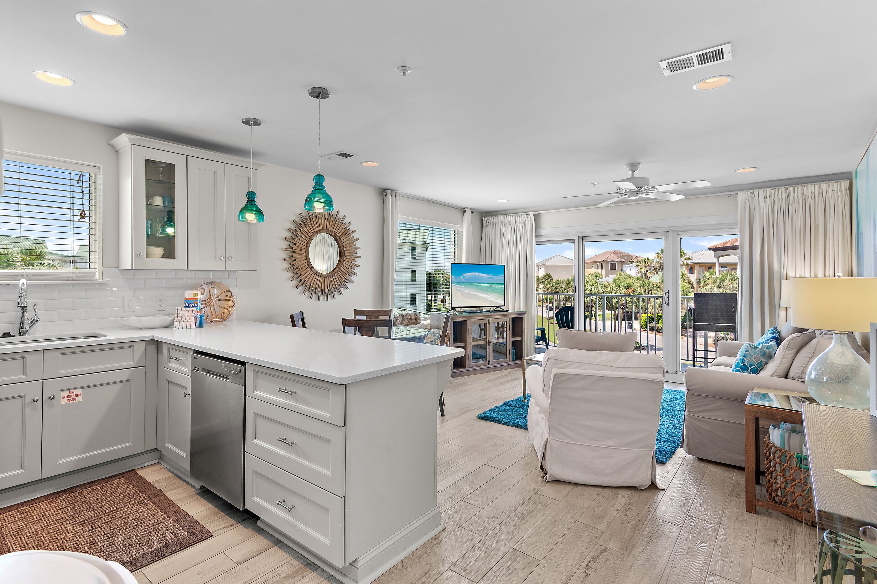 A modern kitchen with white cabinets, a dishwasher, and a large island. There is a dining area with a blue rug and a white sofa.