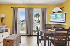 A living room with a sofa, a coffee table, a TV, and a dining area with chairs and a table. - ⭐Across St from Beach Access-FAB Gulf Views-Pool+Hot Tub-Summer Breeze 103⭐ (Miramar Beach)