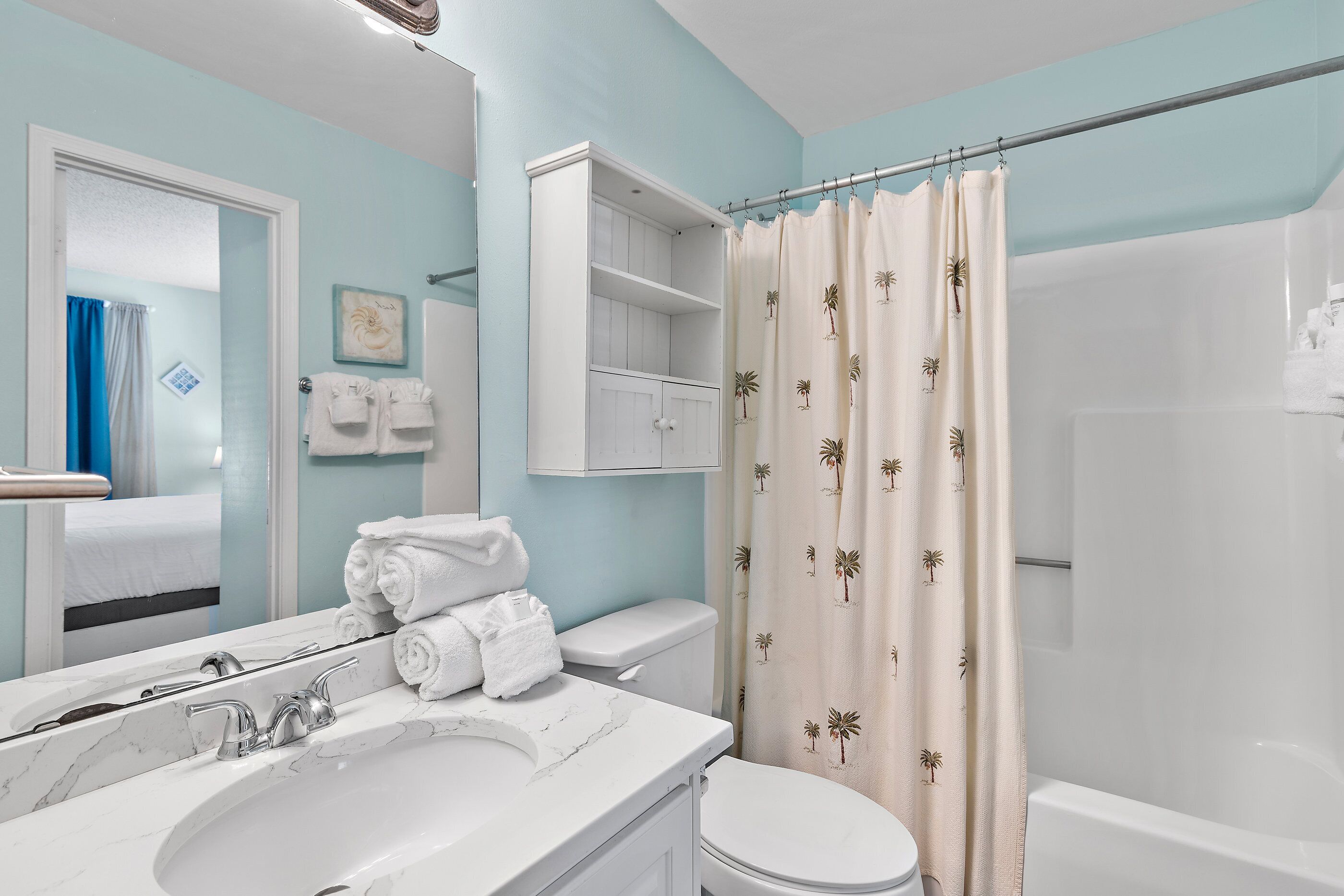 Une salle de bain avec un lavabo blanc, des toilettes et un rideau de douche orné de motifs de palmiers.