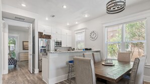 Una cocina moderna con armarios blancos, una mesa de comedor de madera y un reloj en la pared.