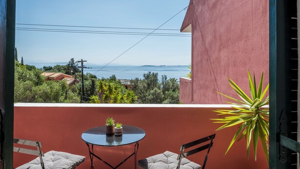Ein Balkon mit Tisch und Stühlen, der Blick auf die Küste mit Vegetation und einer fernen Uferlinie bietet.