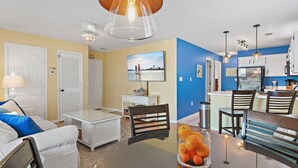 A modern living room with a dining table, chairs, and a kitchen area with cabinets and appliances. - 🌅 Ground Floor Condo~Walk to Beach~St. Martin Beachwalk Villas 214 (Destin)