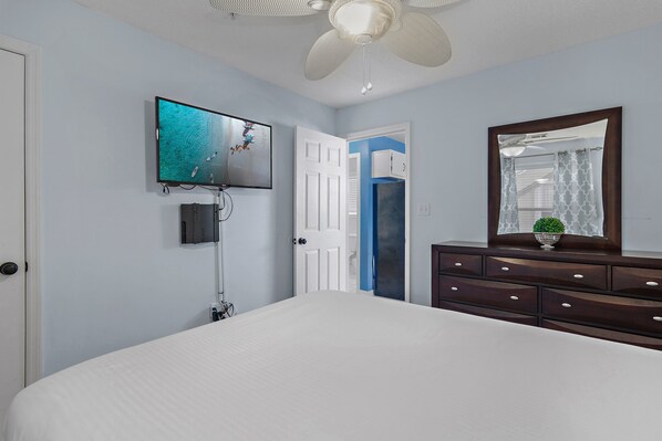 Un dormitorio con una cama, televisor montado en la pared, cómoda y ventilador de techo.