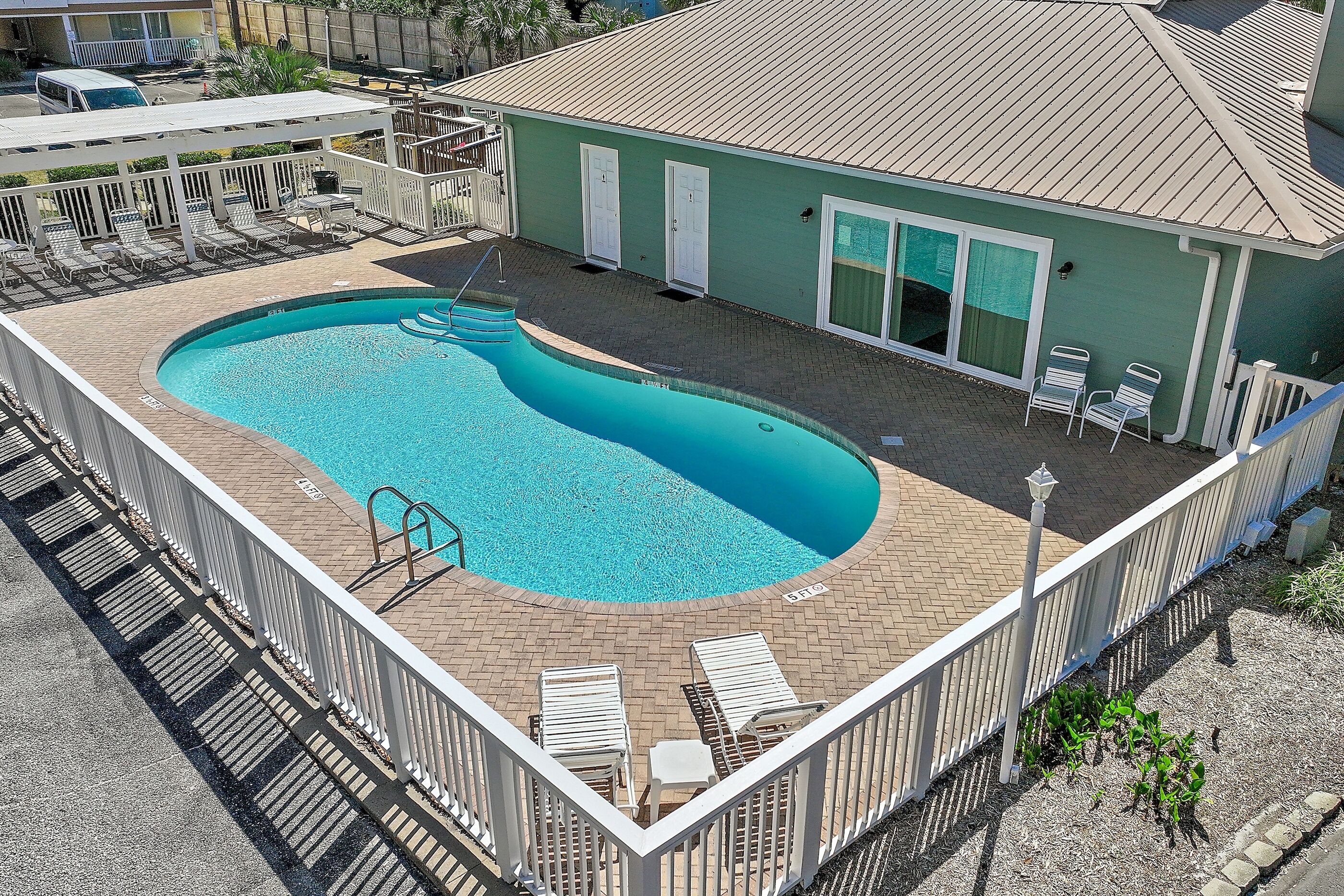 A swimming pool with a deck, lounge chairs, and a building with a green exterior.