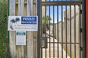 Una entrada con puerta de seguridad a una zona de playa privada, con un letrero que indica que el acceso a la playa es solo para propietarios e invitados.