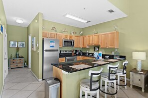 A kitchen with a central island, wooden cabinets, a stainless steel refrigerator, and a microwave. - ☀Across From Beach~Community Pool~ Hot Tub~Caribbean Dunes 203☀ (Destin)