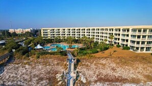 Ein Hotel mit mehreren Stockwerken, einem Schwimmbad und einer angelegten Grünfläche mit Palmen.