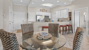 A modern kitchen with white cabinets, a central island, and a glass dining table.