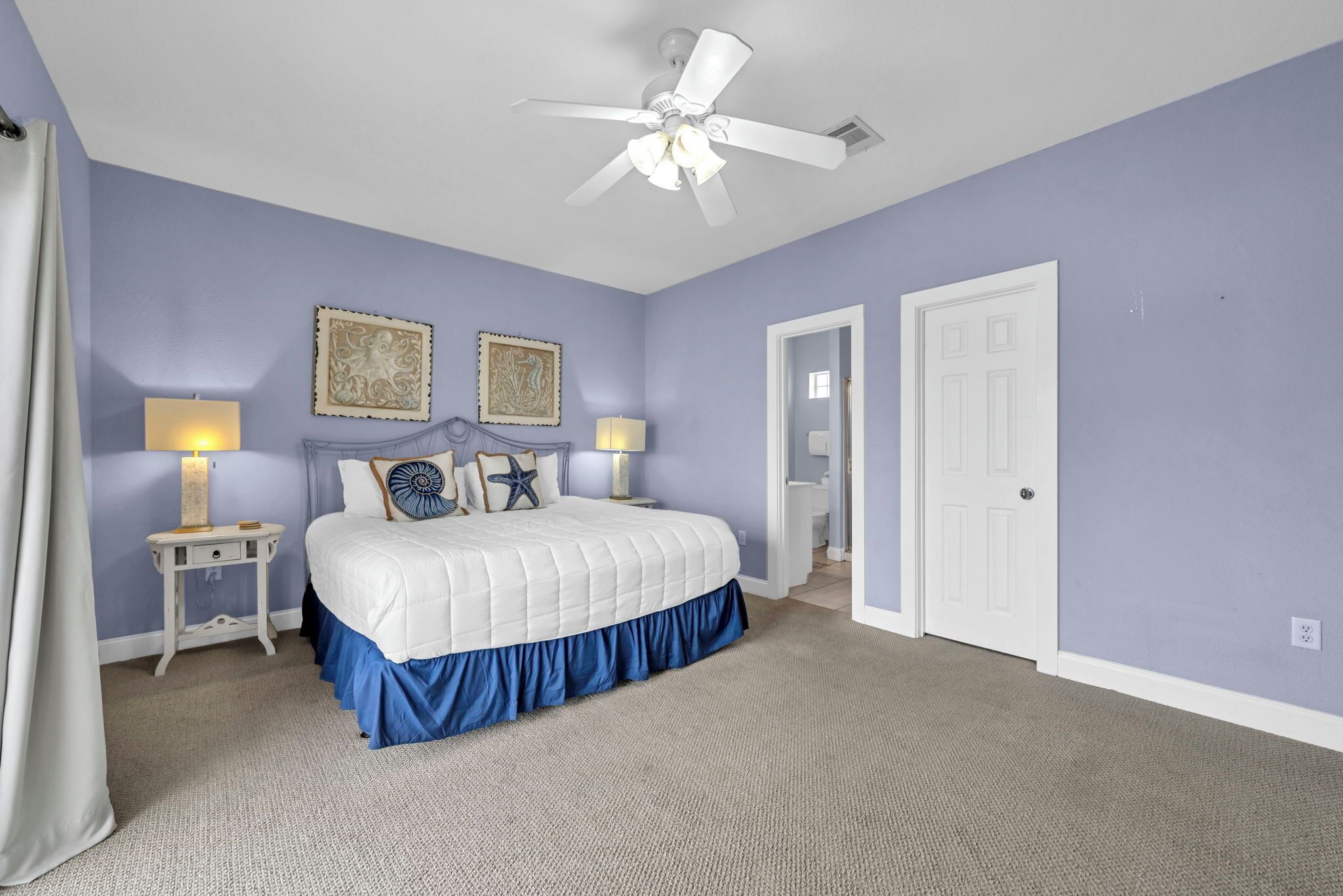 A bedroom with a bed, two bedside tables, a ceiling fan, and a door.