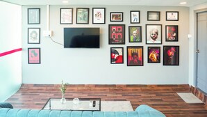 A living room with a flat-screen TV, framed posters on the wall, a blue sofa, and a coffee table with a vase. - Housr 78 Madhapur Hyderabad Hitech City (Hyderabad)