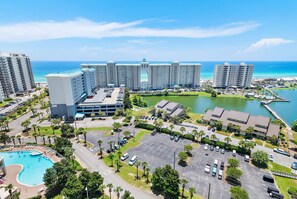 A hotel with multiple buildings, a swimming pool, parking area, and a view of the ocean.
