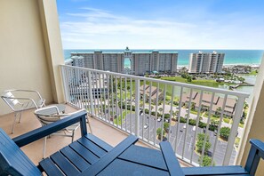 A balcony with a view of the ocean, a parking lot, and hotel buildings.