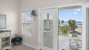 A room with a view of the beach, a white dresser, a plant, and a balcony with a railing.