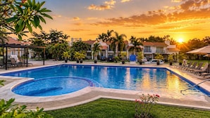 A swimming pool with a sunken area, surrounded by lounge chairs and palm trees, with a backdrop of residential buildings and a sunset. - Relax in Nuevo Vallarta | Pool & Great Location (Nuevo Vallarta)