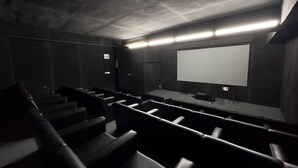 Una sala de cine oscura y moderna con asientos escalonados, una pantalla grande y un proyector.