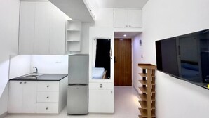 Una cocina compacta con armarios blancos, un lavamanos y un refrigerador.
