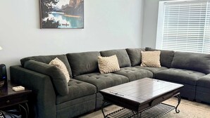 Uma sala de estar com um sofá seccional, uma mesa de centro e um quadro na parede.