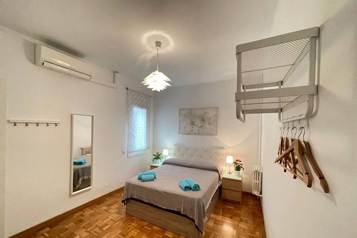 A bedroom with a bed, a hanging light fixture, a window, and a wall-mounted rack.