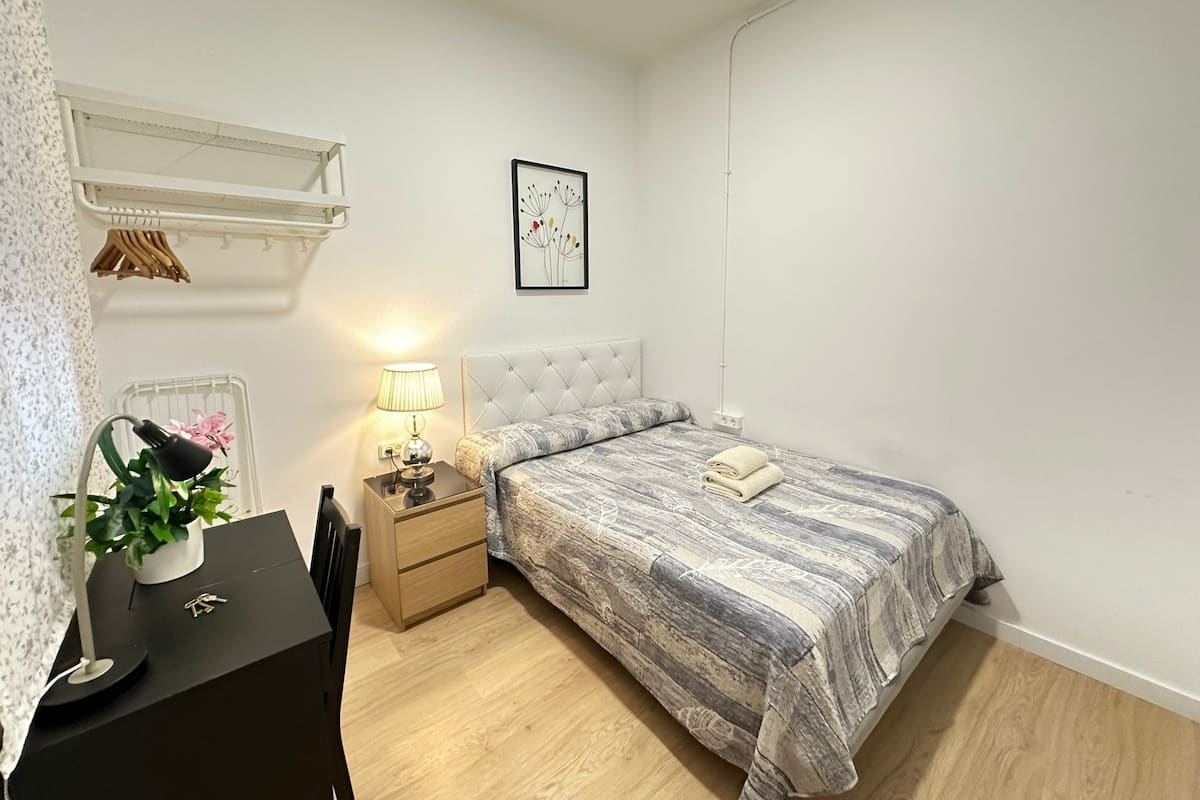 A bedroom with a bed, bedside table, lamp, and a framed picture on the wall.