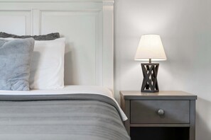 A neatly made bed with a grey and white duvet, a grey throw pillow, and a bedside table with a lamp. - Quittin' Time - Stay for 6 with Golf Course Views & Resort Amenities (Branson)