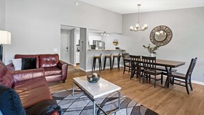 A living room with a leather sofa, a coffee table, and a dining area with a wooden table and chairs. - Quittin' Time - Stay for 6 with Golf Course Views & Resort Amenities (Branson)