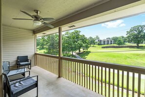 A balcony with a ceiling fan, two chairs, and a view of a golf course and residential buildings. - Quittin' Time - Stay for 6 with Golf Course Views & Resort Amenities (Branson)
