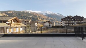 Una terrazza sul tetto con vista su montagne innevate, un'area recintata e edifici tradizionali con balconi.