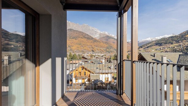 Un balcone con vista su un paesaggio montano, ringhiere in legno e cielo sereno.