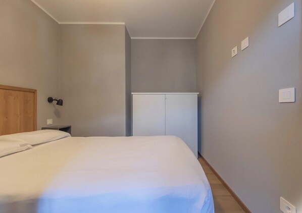Un dormitorio con cama, armario, mesita de noche y lámpara de pared.