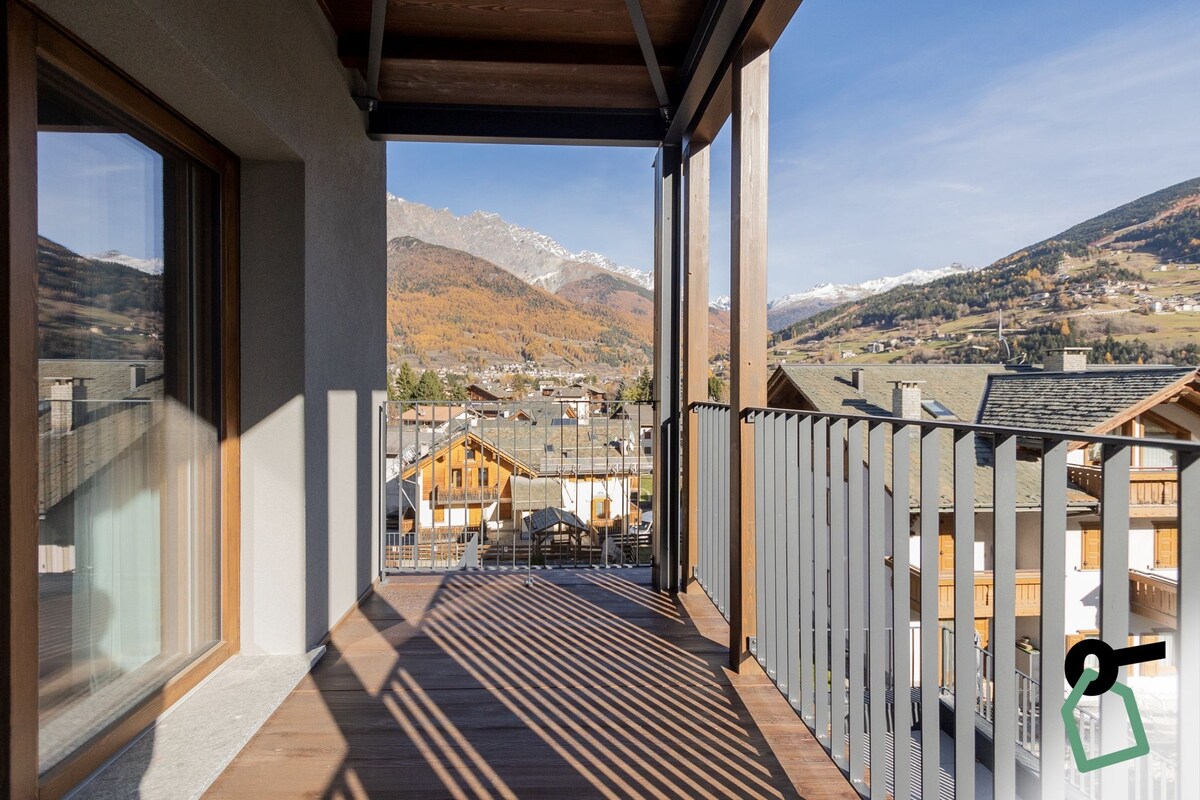 Un balcón con vistas a un paisaje montañoso, edificios de madera y cielo despejado.