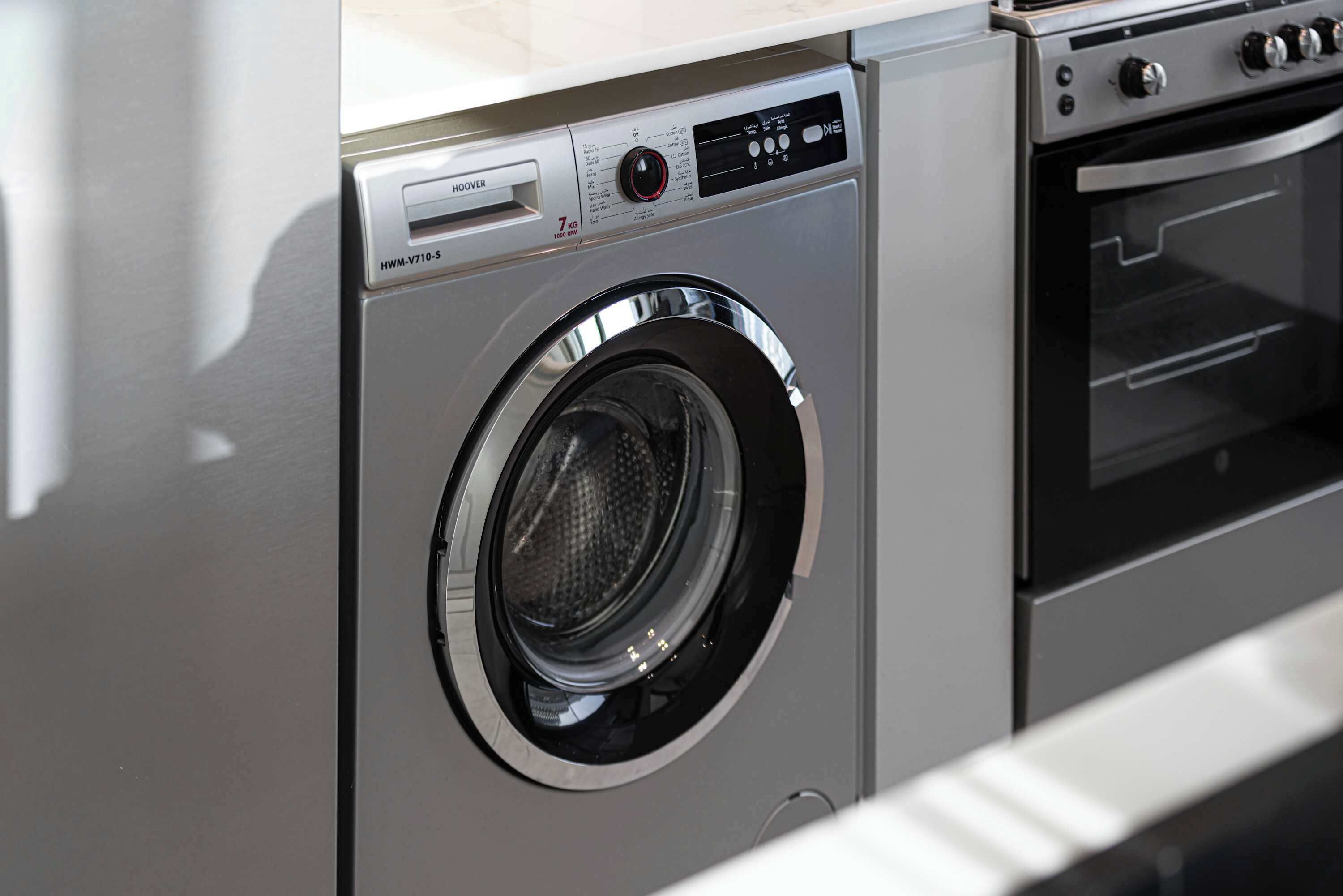 Een voorzichtsweergave van een moderne keuken met een ingebouwde wasmachine en droger, roestvrijstalen apparatuur en een magnetron.