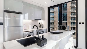 A modern kitchen with stainless steel appliances, a large window, and a view of a building with balconies. - Luxury 2BR with Canal View Burj Khalifa view and Infinity Pool Access (Business Bay)