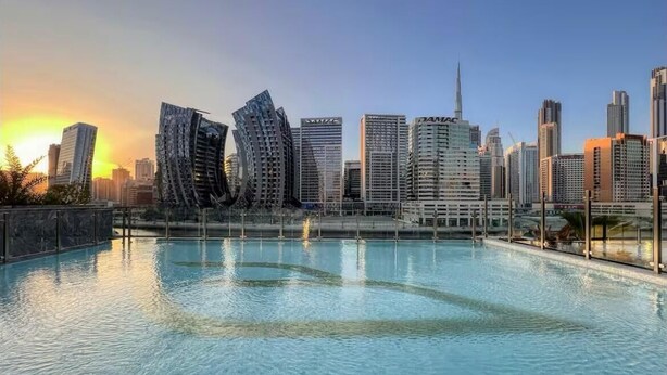 A modern cityscape with skyscrapers and a large swimming pool. - Luxury 2BR with Canal View Burj Khalifa view and Infinity Pool Access (Business Bay)