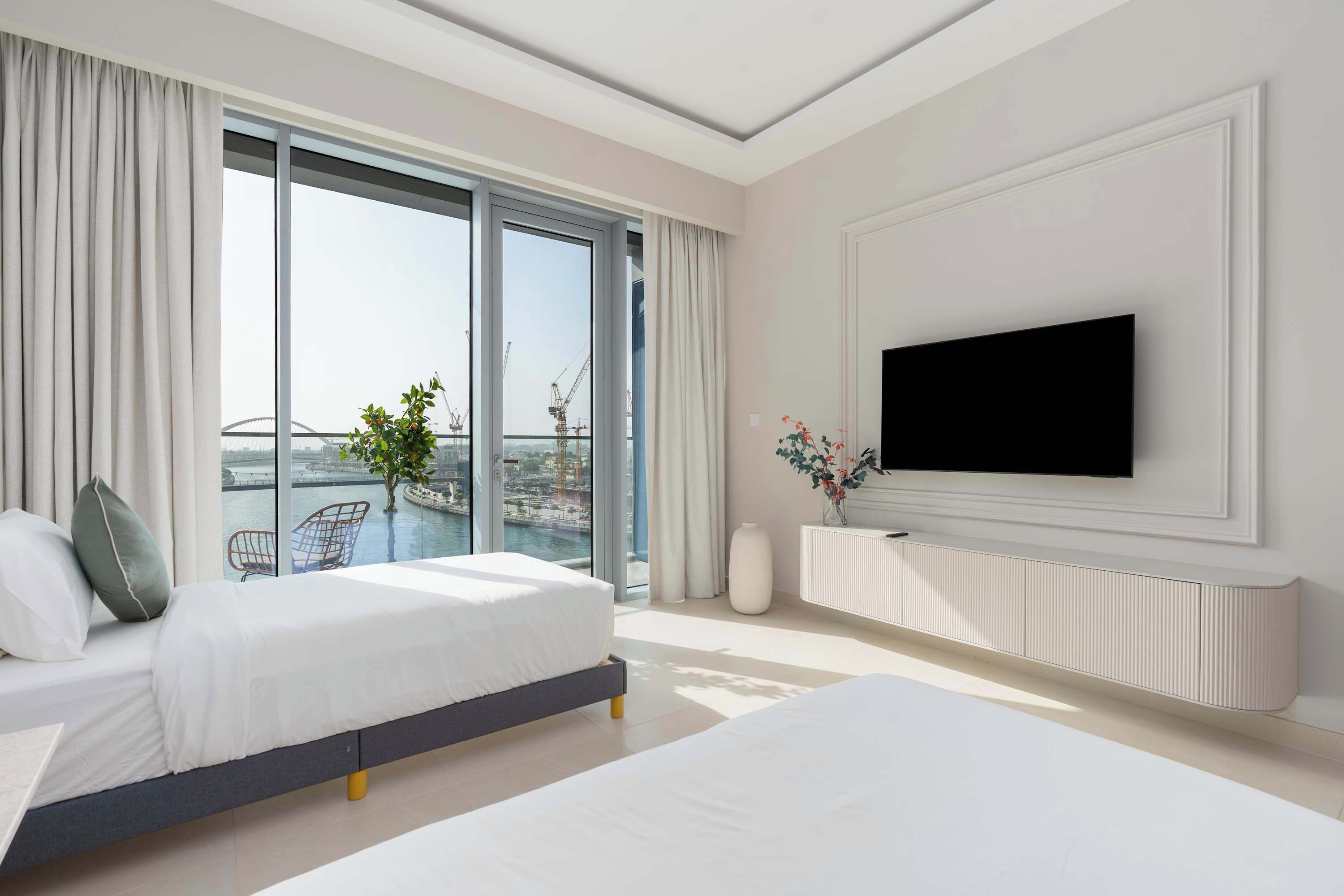 A modern hotel room with a large bed, a TV mounted on the wall, and a balcony with a view of the city.
