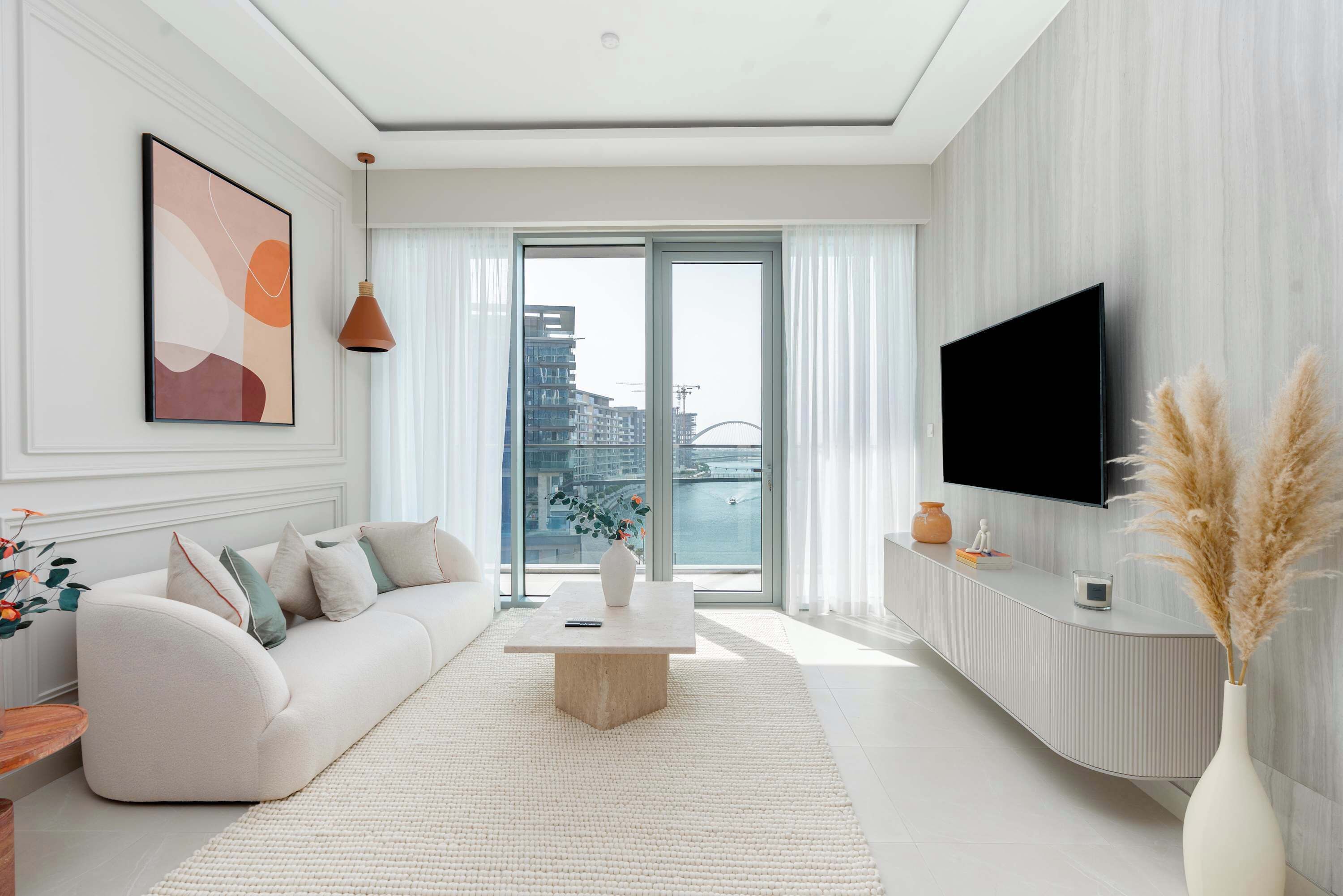 A modern living room with a sofa, a coffee table, a TV, and a view of a cityscape through large windows.